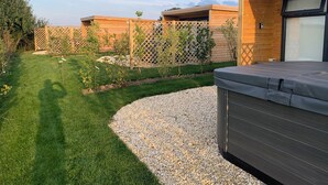Un espace extérieur moderne, aménagé en terrasse, avec un jacuzzi, une plateforme en bois et une pelouse bien entretenue.
