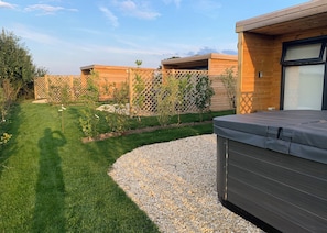 A modern outdoor patio area with a hot tub, a wooden deck, and a well-maintained lawn. - Escape to a quirky, cosy pod designed for the perfect romantic retreat. (Bubwith)