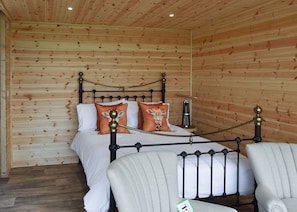 A wooden-paneled room with a bed, two pillows, a nightstand, and a chair. - Escape to a quirky, cosy pod designed for the perfect romantic retreat. (Bubwith)