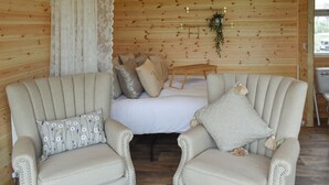 Une pièce confortable avec un lit, deux fauteuils, un rideau en dentelle et une plante fixée au mur.