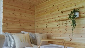 Une pièce de cabane en bois comprenant un lit, des oreillers, une plante suspendue et une étagère avec des verres.