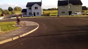Une rue résidentielle avec deux maisons, un rond-point et un fourgon stationné.
