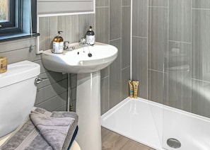 Un baño con un lavamanos pedestal blanco, un inodoro y una bañera. Hay artículos de aseo en el lavamanos y una toalla en el suelo.