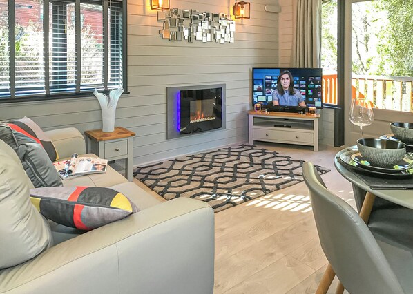 Una sala de estar con chimenea, televisor y comedor con una mesa dispuesta para dos.