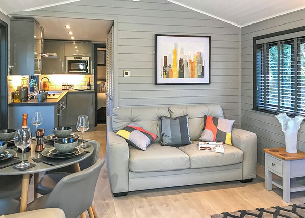 Una sala de estar moderna con un sofá gris, una mesa de comedor con copas de vino y un cuadro con una vista urbana en la pared.