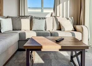 Un salon moderne avec un canapé d’angle, une table basse en bois et une télécommande posée dessus.