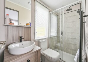Ein modernes Badezimmer mit einem großzügigen Waschbecken, Toilette und einer Duschkabine aus Glas.