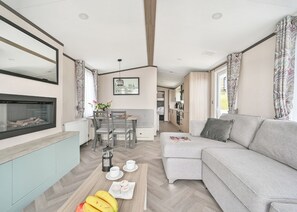 A modern living room with a sofa, a dining table with chairs, a fireplace, and a kitchen area in the background.