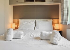 Una cama bien hecha con sábanas blancas y dos toallas enrolladas al pie.