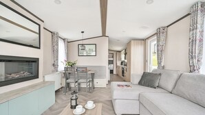 Un salon moderne avec un canapé, une table à manger et des chaises, une cheminée et, au fond, un coin cuisine.