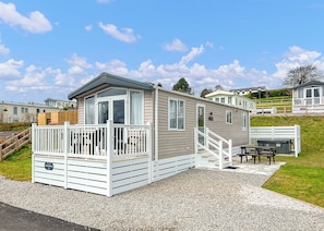 A mobile home with a deck, a covered outdoor seating area, and a gravel driveway.