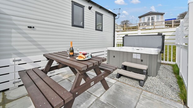 Une maison mobile dotée d’un patio comprenant une table en bois, un jacuzzi et un barbecue.