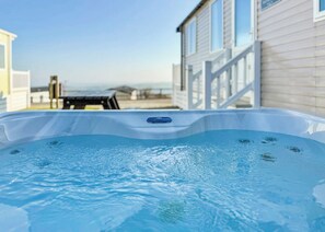 A hot tub with a view of a beach and a house in the background.