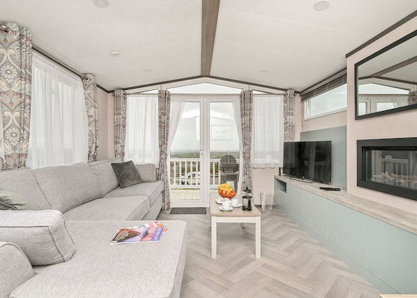 A modern living room with a sofa, coffee table, TV, and a balcony with a view.