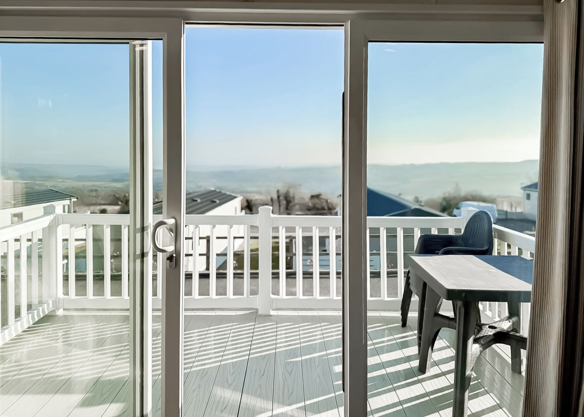 Ein Balkon mit Blick auf das Meer und sanfte Hügel in der Ferne, mit weißem Geländer und einem Tisch mit Stühlen.