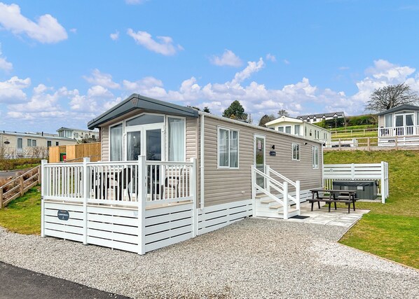 A mobile home with a deck, a covered outdoor seating area, and a gravel driveway.