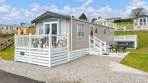 Une maison mobile dotée d’une terrasse, d’un espace extérieur couvert aménagé en coin salon et d’une allée en gravier.