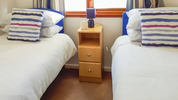 A room with two beds, each with striped pillows, a nightstand with a lamp, and a window with curtains.