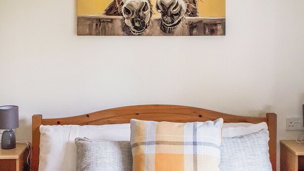 A bed with a wooden headboard, two pillows, and a wall-mounted artwork. - Modern two bedroom lodge, one double and one twin with en suite shower. (Langworth)
