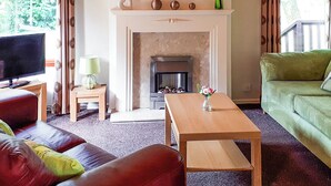A living room with a fireplace, a television, a sofa, a coffee table, and a green couch. - Modern two bedroom lodge, one double and one twin with en suite shower. (Langworth)