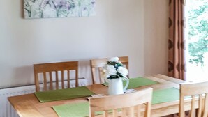 A dining table with green placemats, wooden chairs, and a white vase with flowers. - Modern two bedroom lodge, one double and one twin with en suite shower. (Langworth)