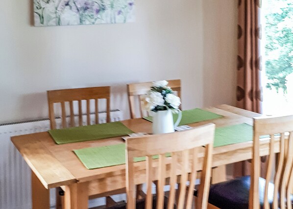 A dining table with green placemats, wooden chairs, and a white vase with flowers.