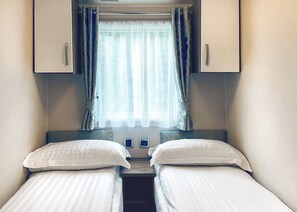 Un dormitorio con dos camas individuales, una ventana con cortinas y una mesita de noche pequeña.