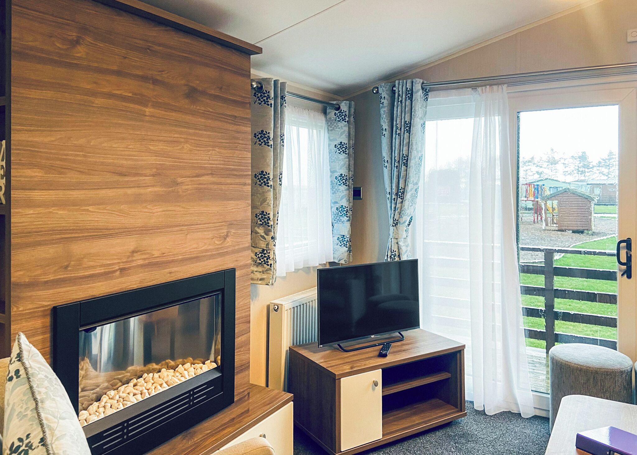 Ein Wohnzimmer mit Kamin, Fernseher, Holzschrank und einer Glasschiebetür, die auf einen Balkon führt.