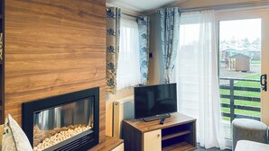 Ein Wohnzimmer mit Kamin, Fernseher, Holzschrank und einer Glasschiebetür, die auf einen Balkon führt.