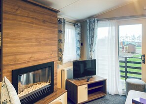 Una sala de estar con chimenea, televisor, aparador de madera y puerta corrediza de vidrio que da a un balcón.