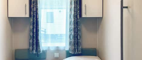 Un dormitorio compacto con dos camas, una ventana con cortinas estampadas y una mesita.