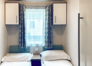 Un dormitorio compacto con dos camas, una ventana con cortinas estampadas y una mesita.