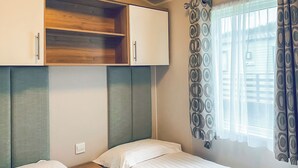 Ein Schlafzimmer mit zwei Einzelbetten, einer Holzregaleinheit und einem Fenster mit gemusterten Vorhängen.