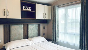 Ein Hotelzimmer mit Bett, Kleiderschrank, Ablagefläche mit einem 'LOVE'-Schild und einem Fenster mit Vorhängen.