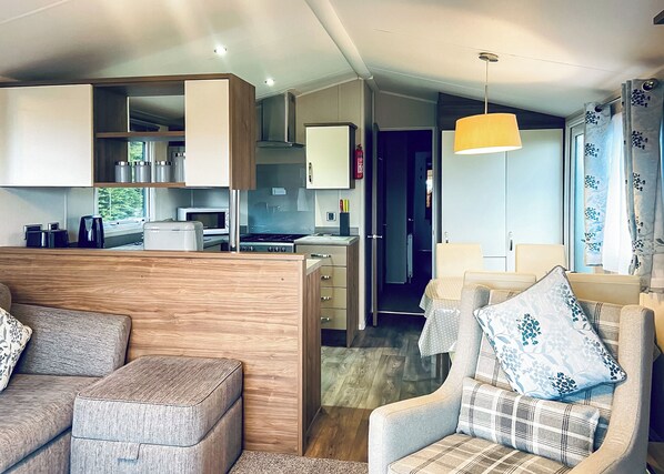 Una sala de estar moderna con sofá, sillones y un comedor, con una cocina al fondo.