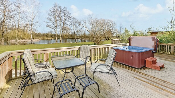 Una terraza con mobiliario exterior, un jacuzzi y vista a un lago.