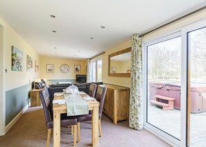 A cozy room with a dining table, chairs, a sofa, a TV, and a large window with curtains. - Luxury lodge with one double and one twin. (Pickering)