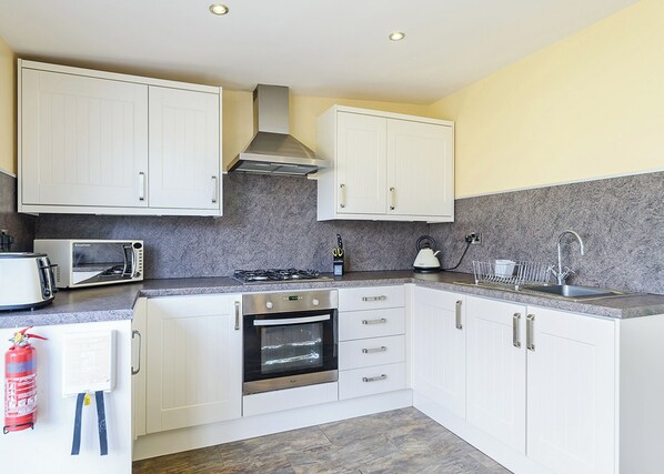 A modern kitchen with white cabinets, a gas stove, a microwave, and a stainless steel range hood.