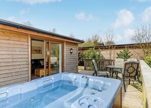 A wooden cabin with a hot tub, patio furniture, and a sliding glass door leading to a deck. - Luxury lodge with one double and one twin. (Pickering)