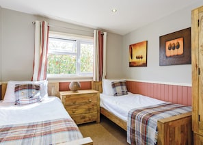 A bedroom with two single beds, a wooden dresser, a window with curtains, and two paintings on the wall.