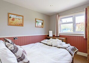 Une chambre à coucher avec un lit, deux tableaux, une table de chevet et une fenêtre avec des rideaux.