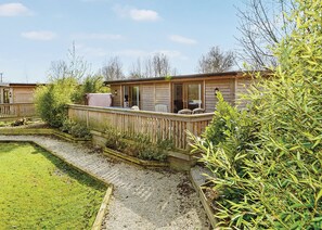 A wooden cabin with a deck, a covered outdoor seating area, and a gravel pathway.