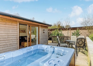 Une cabane en bois dotée d’un bain à remous, de meubles de patio et d’une porte-fenêtre coulissante donnant sur une terrasse.