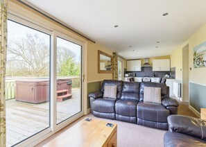 Un salon accueillant avec un canapé en cuir, une table basse en bois et une porte-fenêtre coulissante donnant sur une terrasse dotée d’un jacuzzi.
