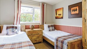 Un dormitorio con dos camas individuales, un aparador de madera, un ventanal con cortinas y dos cuadros en la pared.