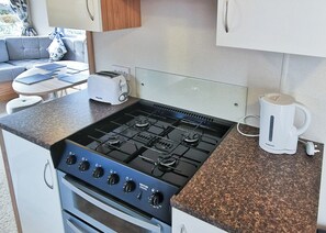 Eine kleine Küche mit Gaskochfeld, Backofen und Kaffeemaschine auf der Arbeitsfläche.