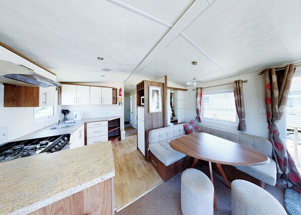 A compact RV interior with a kitchenette, dining area, and seating. - The Gold Plus 2 caravan is 12ft wide with one double and one twin. (Clarach Bay, Nr Aberystwyth)