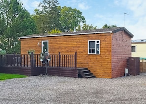 Eine kleine Holzhütte mit einer Holzterrasse und einem eingezäunten Bereich.