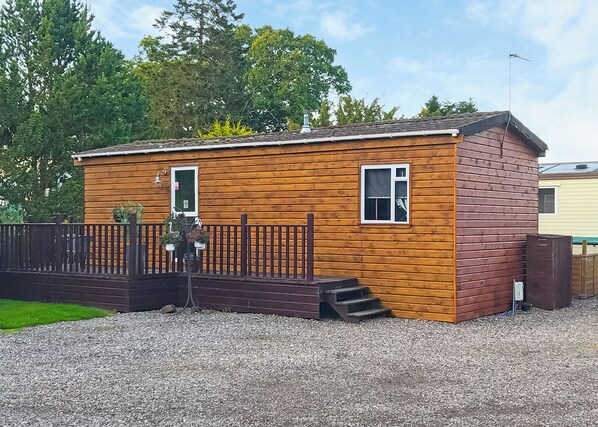 A small wooden cabin with a wooden deck and a fenced area.