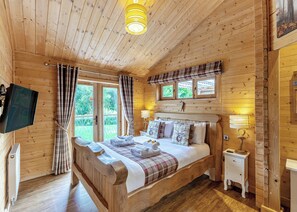 A wooden cabin bedroom with a bed, bedside tables, a television, and a window with curtains.
